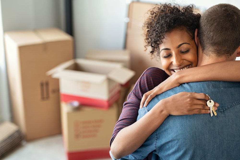 Young african woman holding home keys while hugging boyfriend in their new apartment after buying real estate